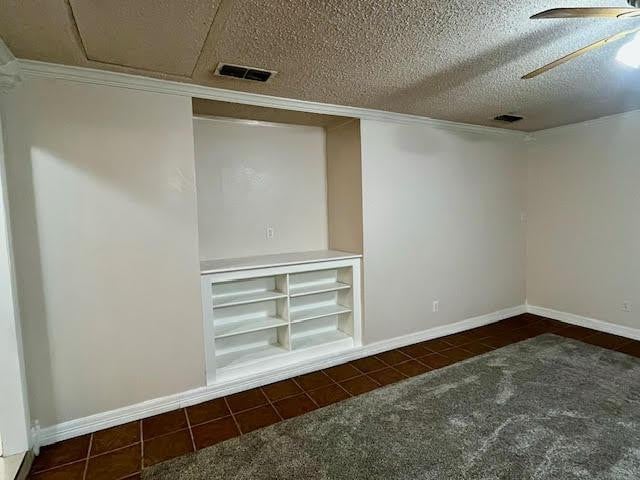 basement featuring dark carpet, a textured ceiling, and ceiling fan