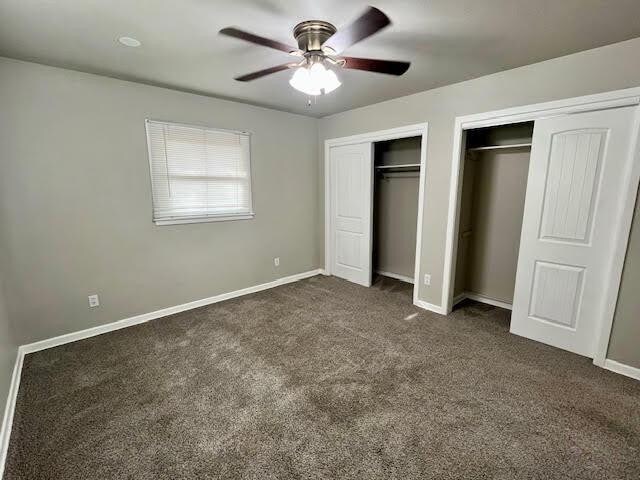 unfurnished bedroom with dark colored carpet, two closets, and ceiling fan