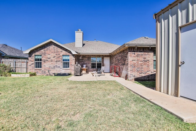 back of property with a lawn, a patio, a chimney, fence, and brick siding