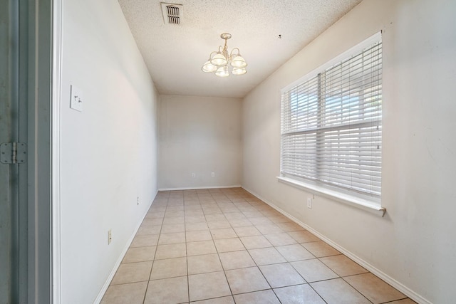 tiled spare room featuring a chandelier and a textured ceiling