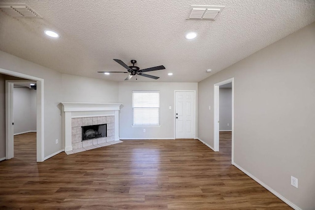 unfurnished living room with a tiled fireplace, ceiling fan, dark wood-type flooring, and a textured ceiling