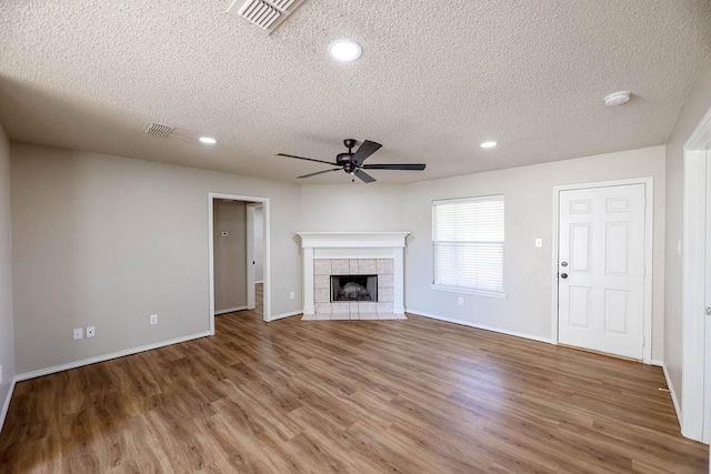 unfurnished living room featuring ceiling fan, wood-type flooring, a fireplace, and a textured ceiling