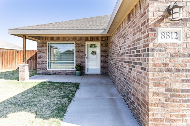 8812 16th St, Lubbock, TX 79416 - property entrance with brick siding, fence, a shingled roof, and a patio