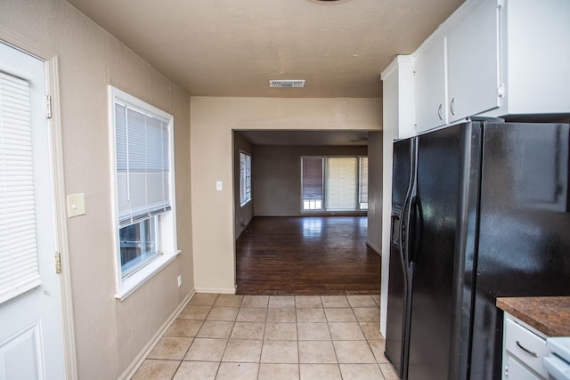 kitchen featuring a healthy amount of sunlight, light tile patterned floors, white cabinets, and black fridge