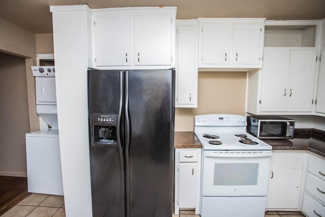 kitchen with light tile patterned floors, white range with electric cooktop, stacked washer / drying machine, white cabinets, and black fridge