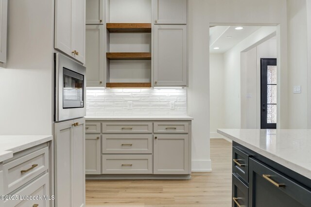 7726 46th St, Lubbock, TX 79407 - kitchen with stainless steel microwave, open shelves, light wood-style floors, backsplash, and light stone counters