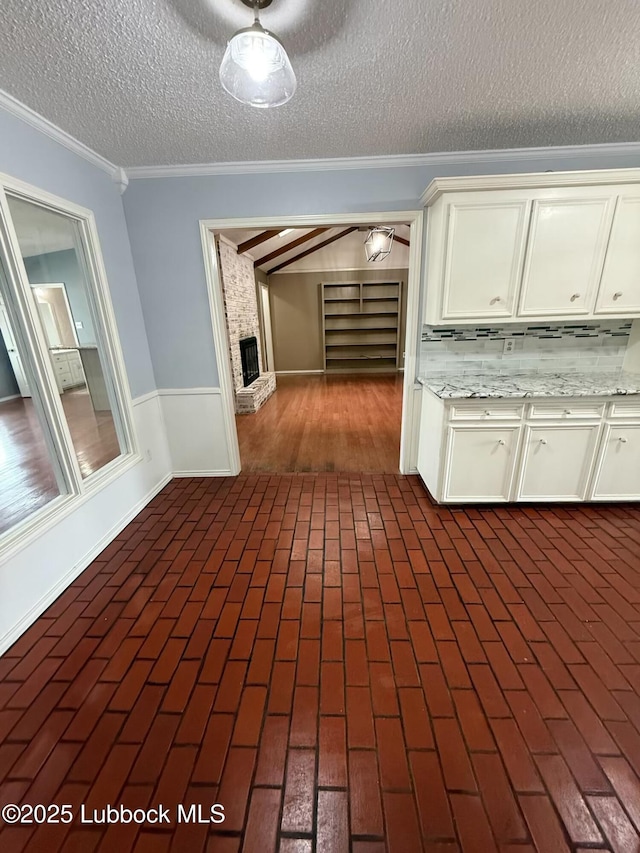 3506 97th St, Lubbock, TX 79423 - kitchen with ornamental molding, a textured ceiling, white cabinetry, a wainscoted wall, and brick floors