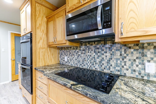 kitchen featuring crown molding, tasteful backsplash, light hardwood / wood-style flooring, dark stone countertops, and black appliances