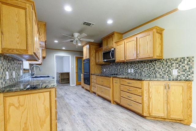 kitchen featuring sink, dark stone countertops, black appliances, crown molding, and light wood-type flooring