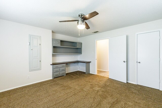 unfurnished office with ceiling fan, light colored carpet, and built in desk