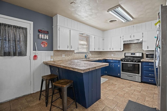 kitchen featuring blue cabinets, a breakfast bar area, white cabinetry, appliances with stainless steel finishes, and kitchen peninsula