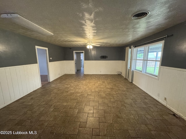 2721 52nd St, Lubbock, TX 79413 - empty room featuring wood walls, a textured ceiling, visible vents, a ceiling fan, and wainscoting
