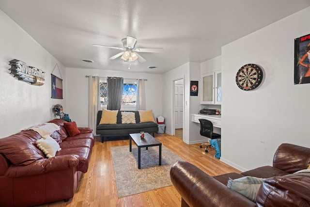 living room with ceiling fan, built in desk, and light hardwood / wood-style flooring