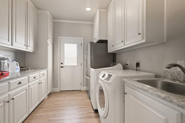 clothes washing area featuring sink, cabinets, ornamental molding, washing machine and clothes dryer, and light hardwood / wood-style floors