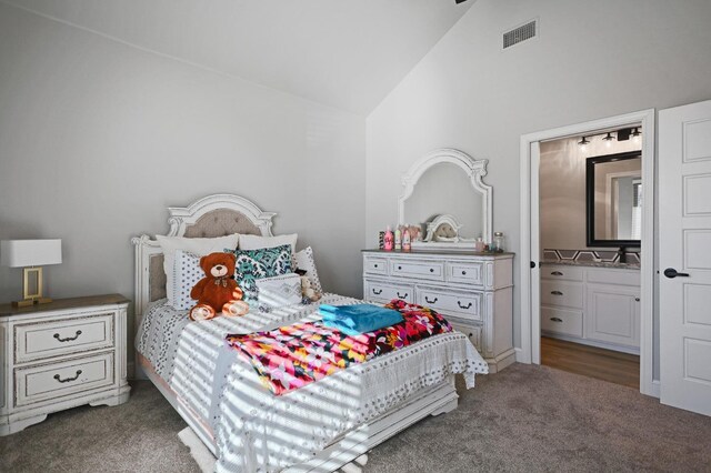 bedroom with lofted ceiling, ensuite bathroom, and dark colored carpet