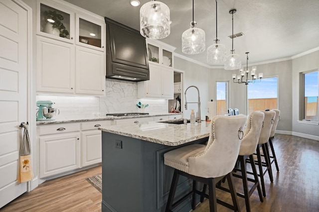 kitchen with pendant lighting, an island with sink, sink, white cabinets, and light stone countertops