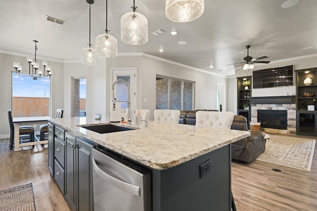 kitchen featuring pendant lighting, sink, a kitchen island with sink, stainless steel dishwasher, and light wood-type flooring