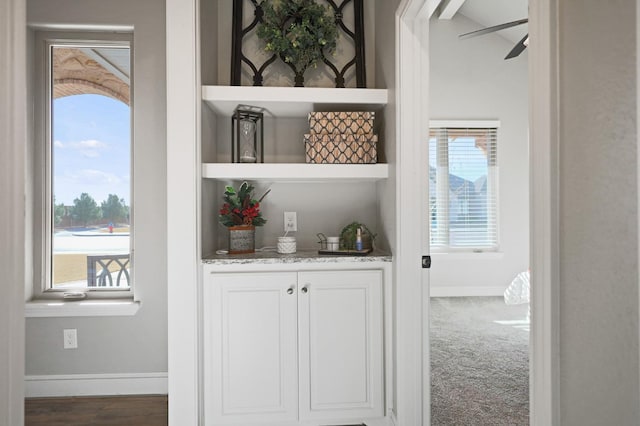 bar featuring light stone counters, ceiling fan, a healthy amount of sunlight, and white cabinets