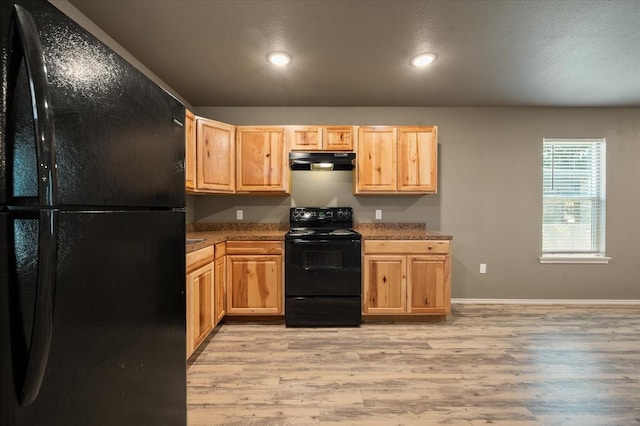 kitchen with dark stone countertops, light brown cabinets, black appliances, and light wood-type flooring