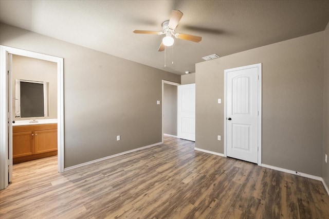 unfurnished bedroom featuring hardwood / wood-style flooring, ceiling fan, ensuite bathroom, and a closet