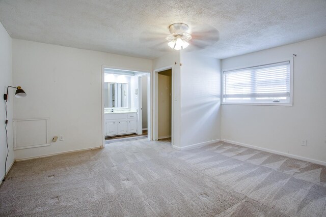 unfurnished bedroom featuring ceiling fan, connected bathroom, light carpet, and a textured ceiling