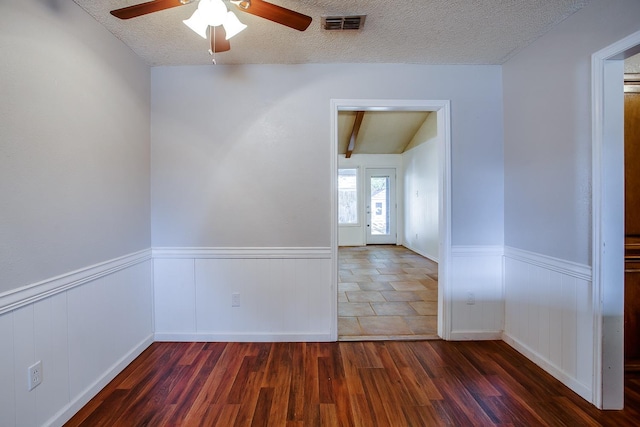 unfurnished room featuring ceiling fan, beam ceiling, dark wood-type flooring, and a textured ceiling