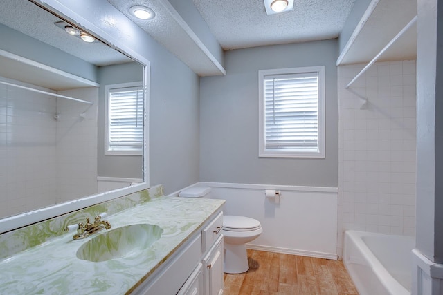 full bathroom featuring hardwood / wood-style floors, tiled shower / bath combo, vanity, a textured ceiling, and toilet