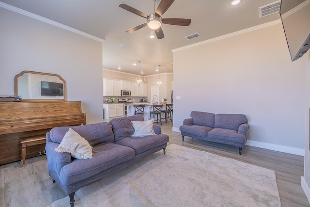 living room featuring visible vents, baseboards, light wood-style floors, and ornamental molding