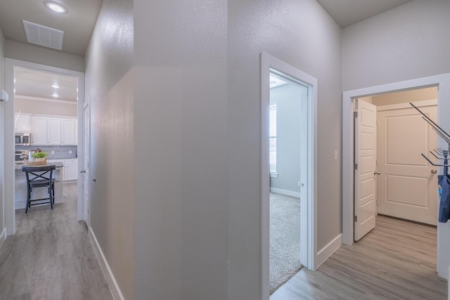 corridor with visible vents, light wood-type flooring, and baseboards