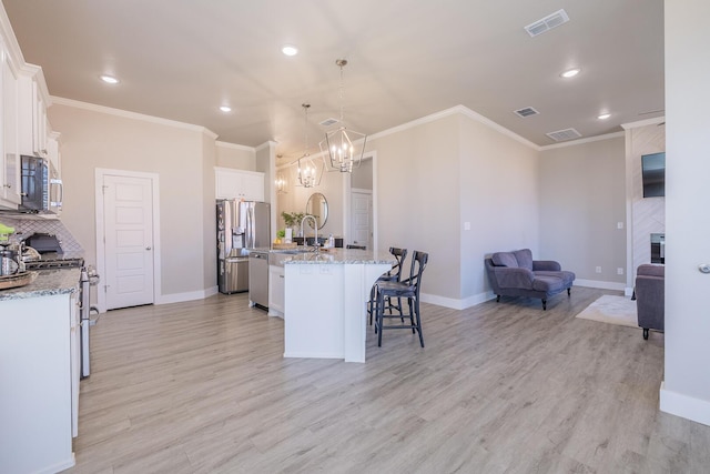 kitchen featuring visible vents, open floor plan, light wood-style floors, appliances with stainless steel finishes, and a breakfast bar area