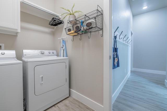 laundry room featuring washing machine and clothes dryer, cabinet space, light wood-style flooring, and baseboards