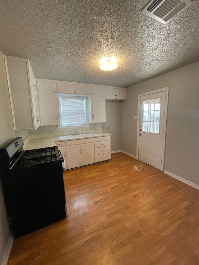 kitchen featuring sink, a textured ceiling, white cabinets, range with gas cooktop, and light wood-type flooring