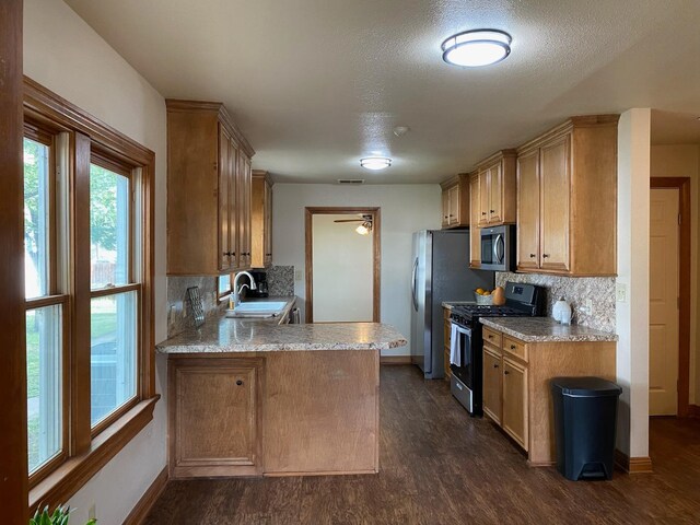 kitchen with sink, dark hardwood / wood-style floors, kitchen peninsula, stainless steel appliances, and backsplash