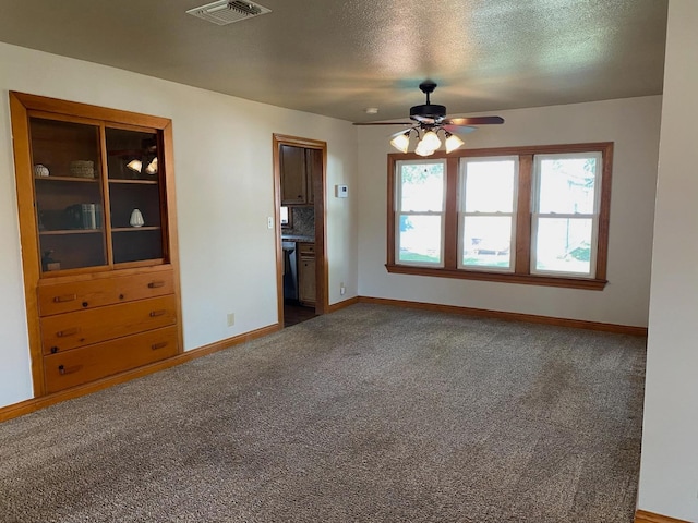 empty room featuring ceiling fan, dark carpet, and a textured ceiling