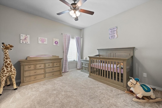 carpeted bedroom featuring baseboards, a crib, and a ceiling fan