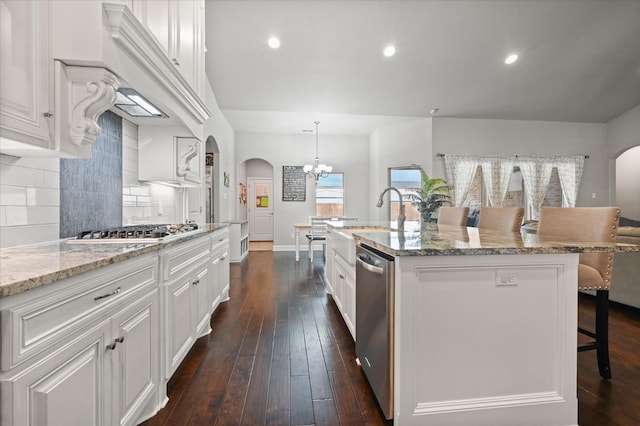 kitchen with appliances with stainless steel finishes, white cabinets, decorative backsplash, hanging light fixtures, and a kitchen island with sink