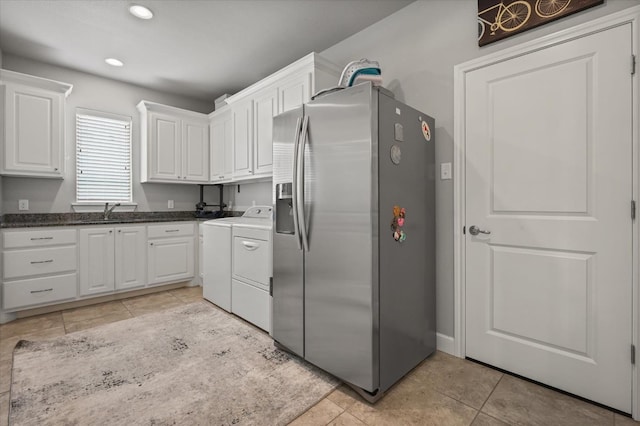 kitchen with light tile patterned flooring, a sink, white cabinetry, stainless steel fridge, and washer and clothes dryer