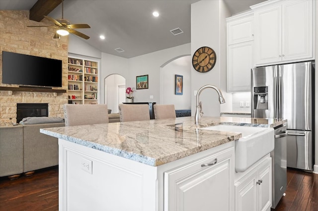 kitchen featuring arched walkways, vaulted ceiling with beams, stainless steel appliances, and dark wood-style flooring