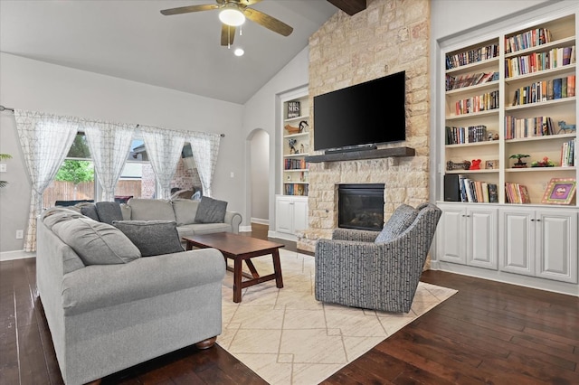 living room featuring built in features, ceiling fan, vaulted ceiling with beams, a fireplace, and light wood-type flooring