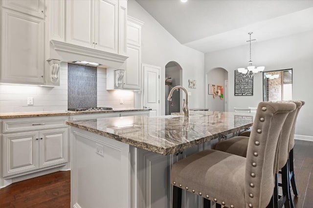 kitchen with lofted ceiling, a kitchen island with sink, light stone countertops, white cabinets, and decorative light fixtures