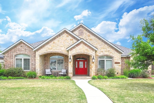 french country inspired facade featuring brick siding, roof with shingles, and a front yard