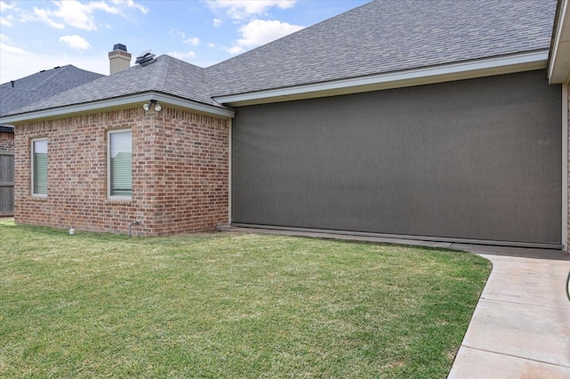 view of side of property featuring a yard, brick siding, a chimney, and a shingled roof