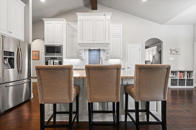 kitchen featuring light stone counters, lofted ceiling, dark wood-style flooring, arched walkways, and appliances with stainless steel finishes