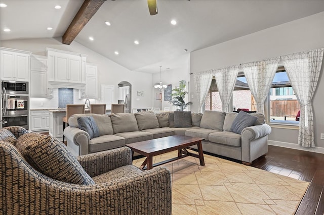 living area with ceiling fan with notable chandelier, lofted ceiling with beams, wood finished floors, arched walkways, and baseboards