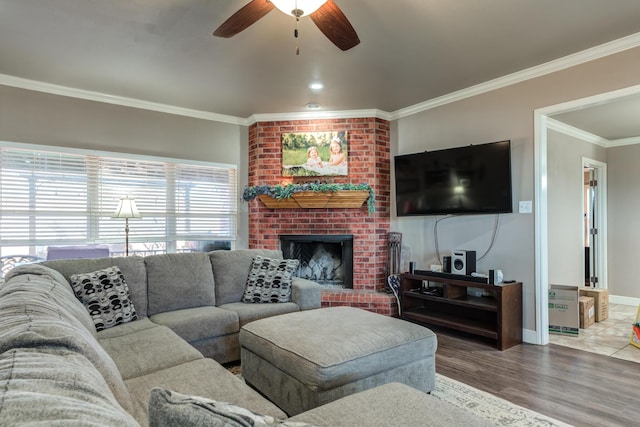 living room with crown molding, a brick fireplace, a ceiling fan, baseboards, and wood finished floors
