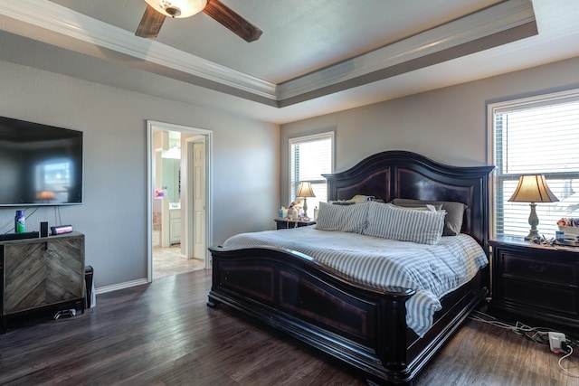bedroom featuring a raised ceiling, crown molding, wood finished floors, baseboards, and ensuite bath