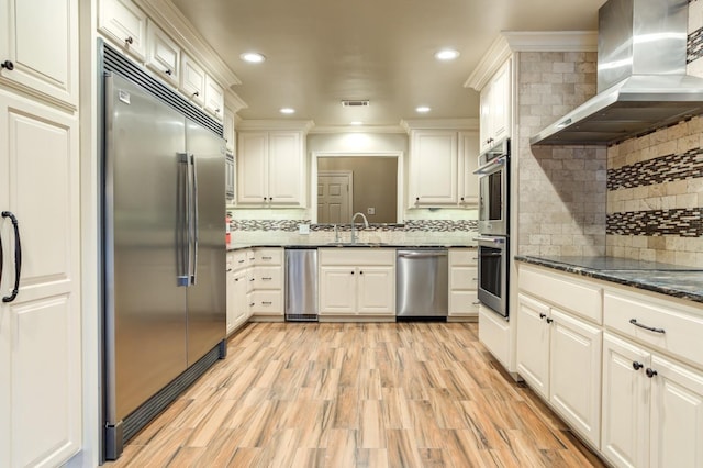 kitchen featuring sink, dark stone countertops, range hood, stainless steel appliances, and light wood-type flooring