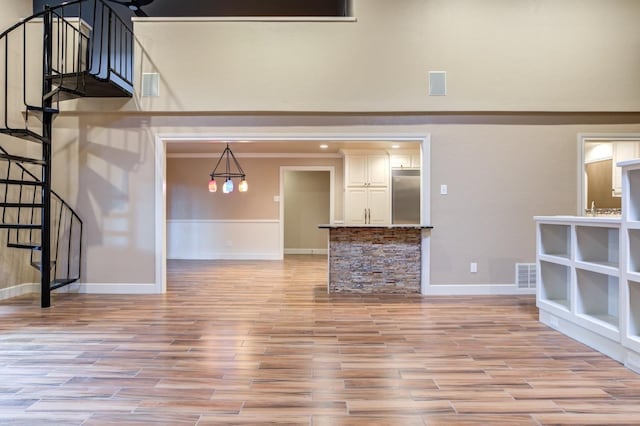 unfurnished living room with a high ceiling, crown molding, and light hardwood / wood-style floors