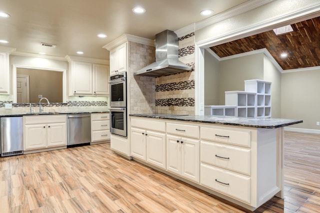 kitchen featuring sink, white cabinets, dark stone counters, stainless steel appliances, and wall chimney exhaust hood