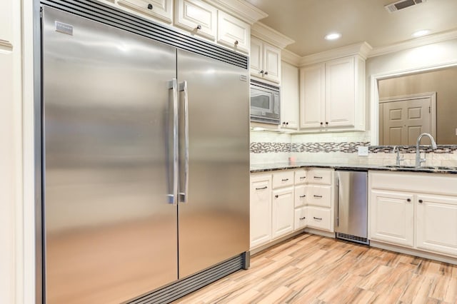 kitchen with white cabinetry, sink, built in appliances, and dark stone counters